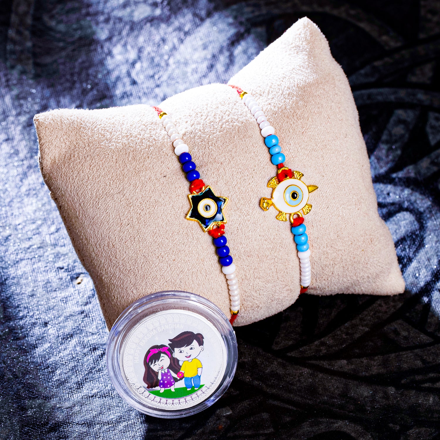 Sukkhi Exclusive Gold Plated Evil Eye Meenakari Rakhis Set of 2 & 2 Gram 999 Pure Silver Coin Combo with Roli Chawal and Rakhi Greeting Card